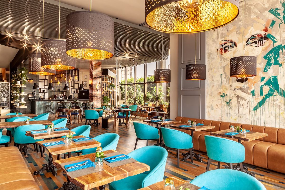 Inspiration photo: a dining room with teal chairs, brass lamps, and a painted mural